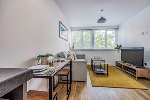 Ein modernes Wohnzimmer mit Sofa, Fernseher, Couchtisch und einem Essbereich mit Tisch und Stühlen.