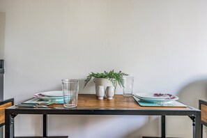 Ein Esstisch mit einer Topfpflanze, zwei Salz- und Pfefferstreuern, einem Glas und einem Teller mit floralem Dekor.
