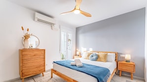 Een slaapkamer met een bed, houten nachtkastjes, een plafondventilator en een raam met uitzicht.