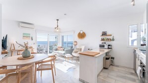Een moderne keuken met een centraal eiland, een eetgedeelte met een ronde tafel, en een woongedeelte met een bank en stoelen.