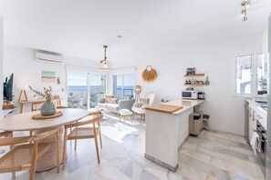 Et moderne køkken med en central ø, et spiseområde med et rundt bord og en opholdsstue med sofa og stole.
