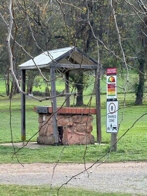 A gazebo structure with a stone base and metal roof, a shared zone sign indicating a speed limit of 8, and a warning sign about a dangerous animal.