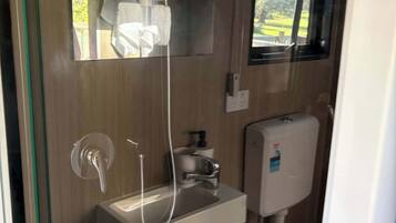 A modern bathroom with a glass shower enclosure, a sink with a faucet, and a toilet with a soap dispenser.