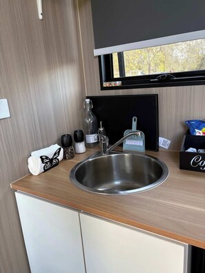 A modern kitchen with a stainless steel sink, a blackboard, and a window with a view of trees.