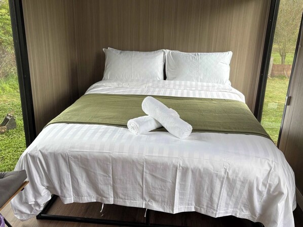A bed with white linens, a green throw blanket, and two rolled towels.