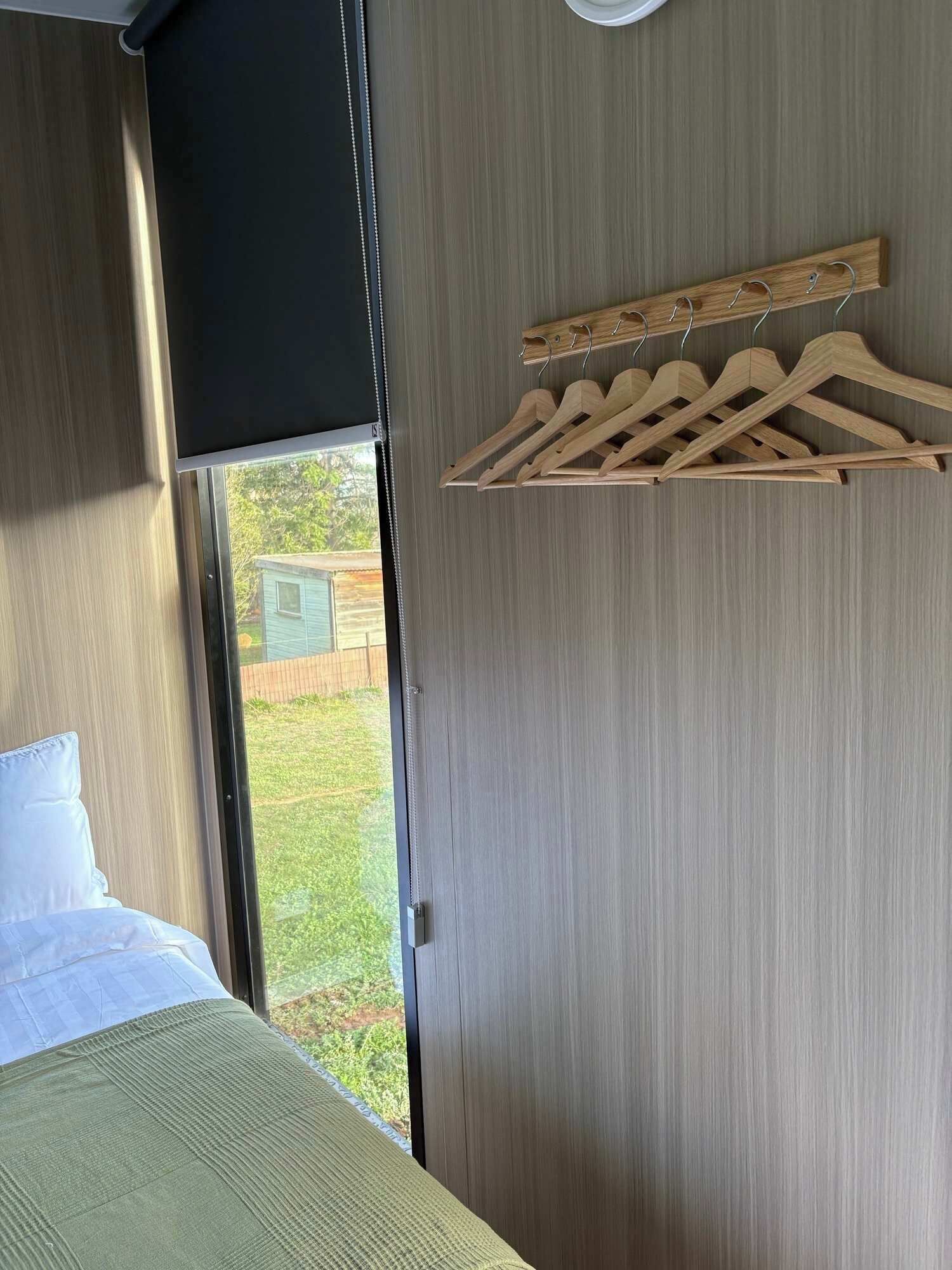 A bedroom with a bed, a window, and a wooden hanger rack.. Whispering Wetlands by Tiny Away