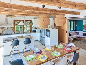A modern kitchen with a central island, dining table set for six, and a living area with a sofa and a large window. - Grande Bastide by Interhome (Mougins)