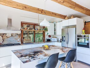 A modern kitchen with a central island, white cabinetry, a built-in stove, and a stainless steel refrigerator. - Grande Bastide by Interhome (Mougins)