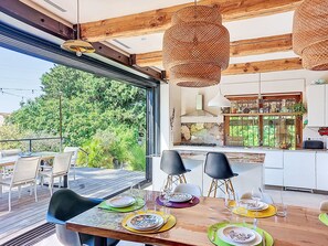 A modern kitchen with a large window, dining area with chairs, and a view of greenery. - Grande Bastide by Interhome (Mougins)