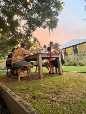 A group of people seated at a wooden table outdoors with string lights overhead.