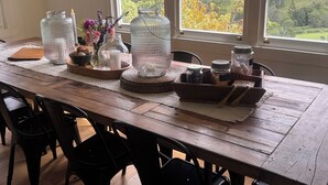 Un tavolo da pranzo in legno con barattoli di vetro, candele e vista su una foresta attraverso ampie finestre.