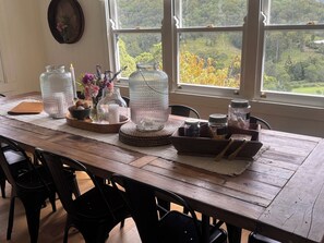 A wooden dining table with glass jars, candles, and a view of a forest through large windows.