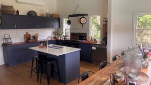 Una cucina con isola centrale, mobili in blu scuro, un piano di lavoro bianco e un tavolo da pranzo in legno con sedie.