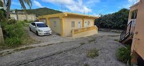 A yellow building with a white car parked in front, surrounded by greenery and a hilly background. - COZYHUB -B (philipsburg)