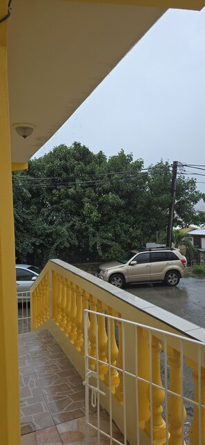 A yellow balcony with a railing, a parked SUV, and a tree in the background. - COZYHUB -B (philipsburg)