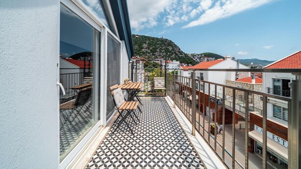 Un balcone con pavimento decorato, un tavolo e sedie, affacciato su una strada con edifici e una collina.