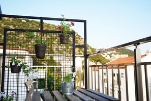 A balcony with a metal grid, wooden bench, and potted plants. - İsinda Pansiyon (Kaş)