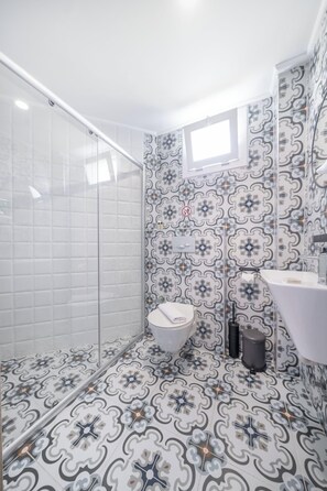 A bathroom with patterned tiles, a toilet, a sink, and a shower area. - İsinda Pansiyon (Kaş)