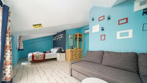 Una stanza con un letto, un divano grigio, un piccolo tavolo bianco e un armadietto in legno.