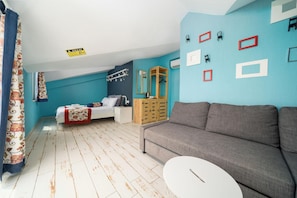 A room with a bed, a grey sofa, a small white table, and a wooden cabinet. - İsinda Pansiyon (Kaş)
