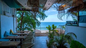 Un restaurante con terraza al aire libre que da al mar, con mesas y sillas de madera, plantas en macetas y vistas al océano.