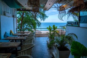A restaurant with outdoor seating overlooking the sea, featuring wooden tables and chairs, potted plants, and a view of the ocean. - Trinco Beach by DSK (Trincomalee)