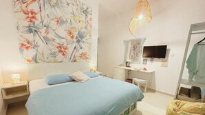 Un dormitorio con cama, mesitas de noche, cómoda, espejo, televisor e lámpara colgante.