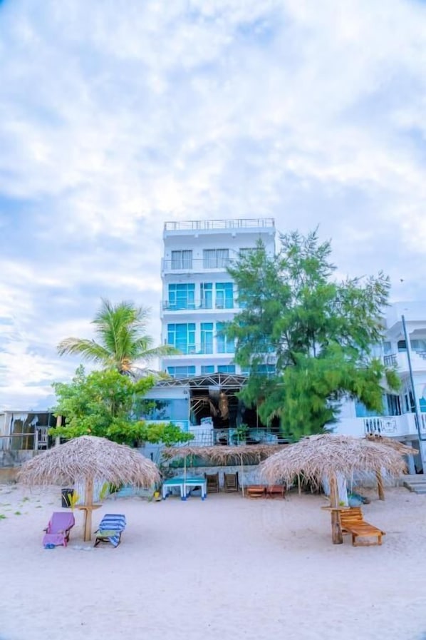 A beachfront hotel with a multi-story structure, outdoor seating with thatched umbrellas, and a sandy beach. - Trinco Beach by DSK (Trincomalee)