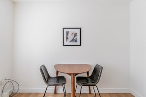 A dining area with a wooden table and two black chairs, a framed picture on the wall, and a white wall. - Blueground | Denny Triangle, view, nr Seattle Art Museum (Seattle)