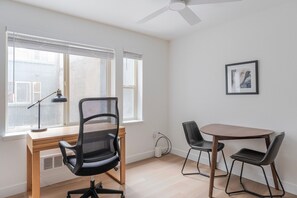 Ein Zimmer mit Schreibtisch, zwei Stühlen, einem Deckenventilator und einem gerahmten Bild an der Wand.