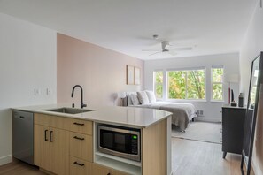 A modern kitchen with a built-in microwave, a dishwasher, and a sink. There is a bed with a view of trees through the window. - Blueground | Denny Triangle, fitness center, nr Seattle Art Museum (Seattle)