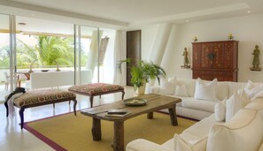 A spacious living area with a white sofa, a wooden coffee table, and a dining table with chairs. There is a large window providing a view of palm trees.
