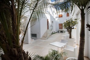 A modern interior with a central staircase, white walls, and a mix of indoor and outdoor plants. - Le Ancore Luxury Apartments (Favignana)