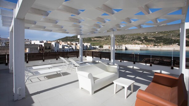 Un área de estar al aire libre con mobiliario blanco y vistas al mar.