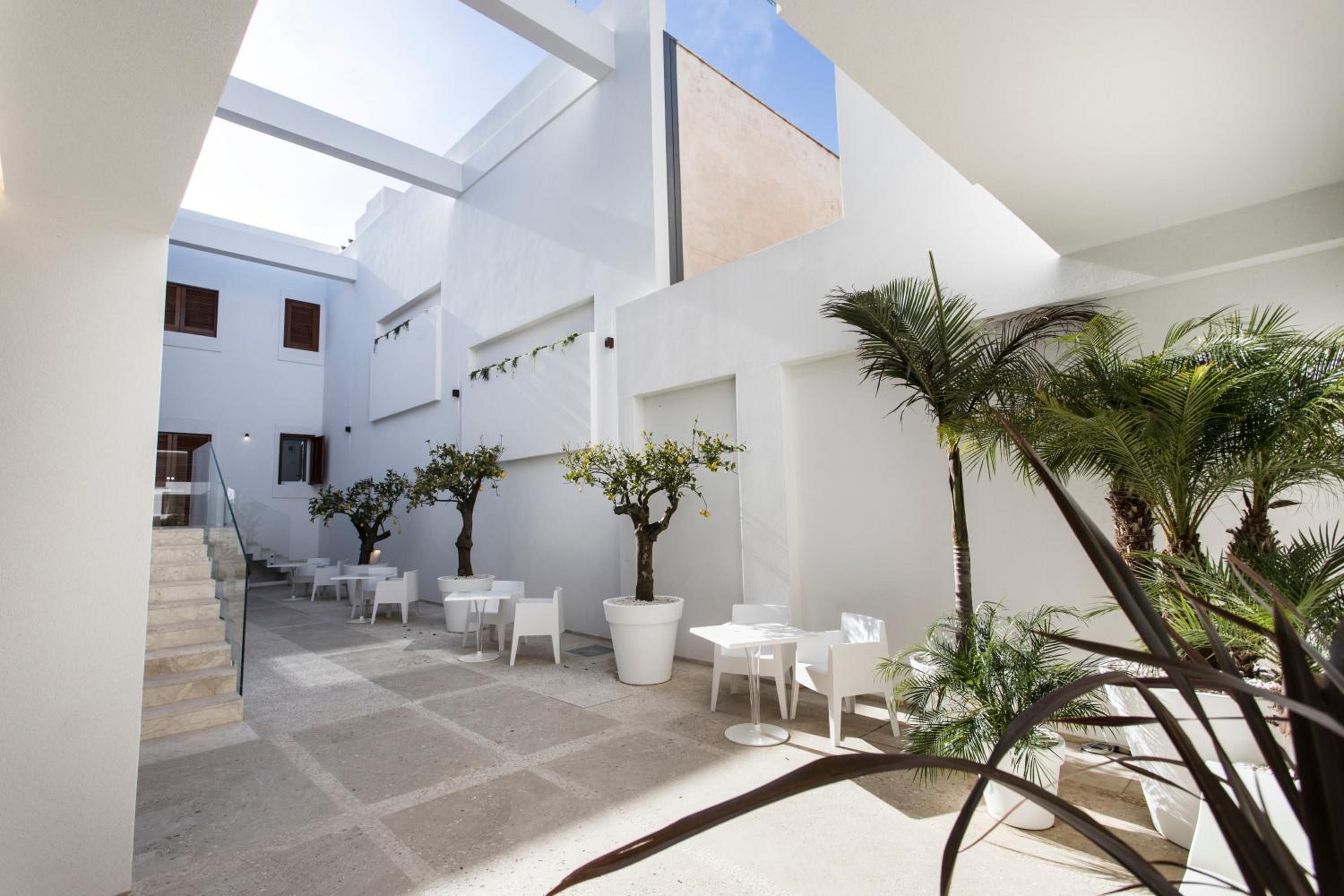 Una moderna area patio esterna con mobili bianchi, piante in vaso e una scala che conduce a un livello superiore.
