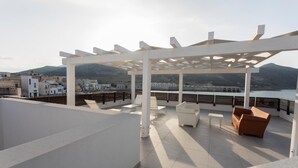 Una terraza en la azotea con pérgola, zona de estar y vistas al mar y edificios.