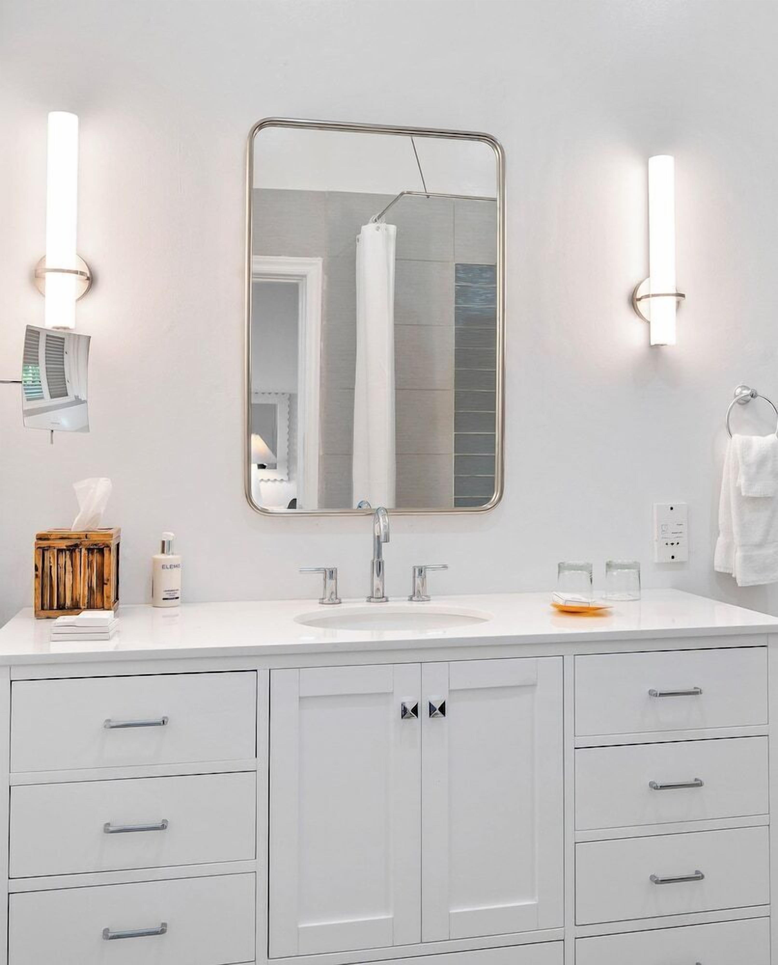A modern bathroom with a large mirror, white cabinets, and a sink.