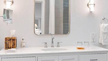 A modern bathroom with a large mirror, white cabinets, and a sink.