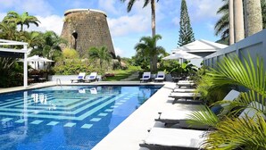 Una piscina con sillas de descanso, palmeras y una torre de piedra histórica.