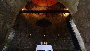 Un comedor subterráneo con paredes de piedra, una mesa dispuesta con velas y una lámpara colgante.