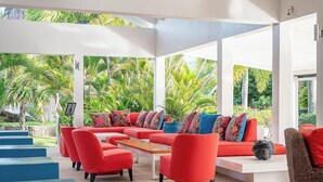 Un área de descanso al aire libre moderna con asientos rojos, una mesa de centro de madera y vistas a exuberante vegetación.