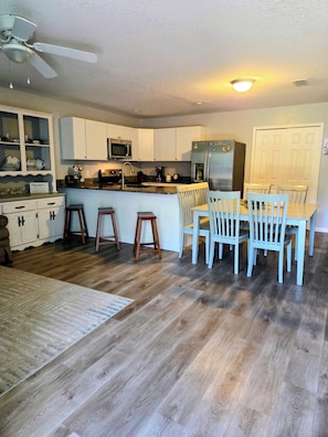 A kitchen with white cabinets, a microwave, a refrigerator, and a dining area with chairs and stools. - Rest and Relaxation! Home away from home! Pet friendly! Convenient location! (St. Augustine)