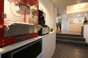 Zona de recepción de un hotel con una máquina de café, un microondas y una escalera que lleva al mostrador de información.