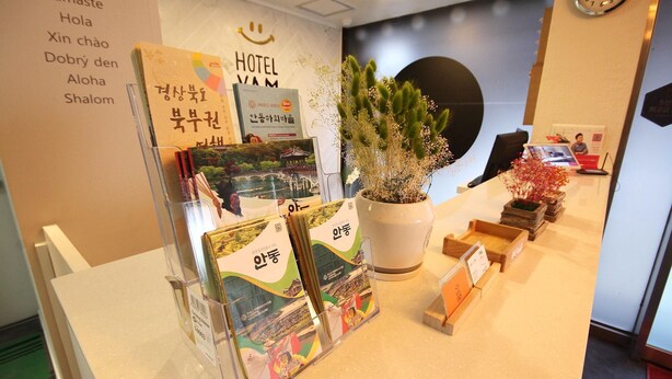 A reception desk with a clock, a wall with multilingual greeting signs, and a potted plant. - Hotel Yam Andong (Andong)