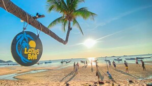 Escena de playa con un letrero que dice 'Lotus Bar' y palmeras.
