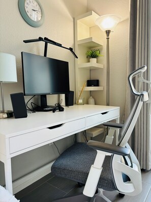 Et moderne skrivebord med en fladskærm, højttalere og en skrivebordslampe.