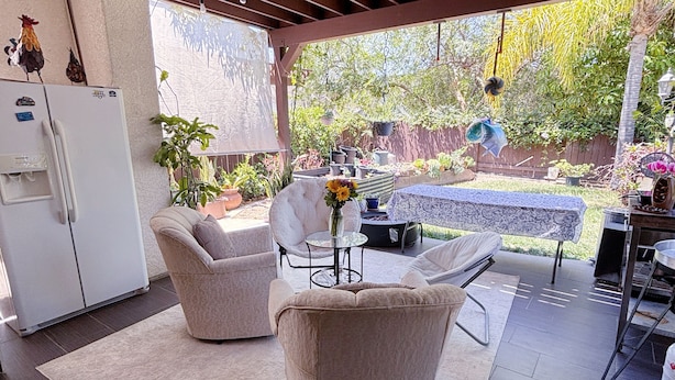 A covered patio with two chairs, a table, a refrigerator, and a view of a garden. - Your cozy getaway awaits in San Diego at this delightful house. (San Diego)