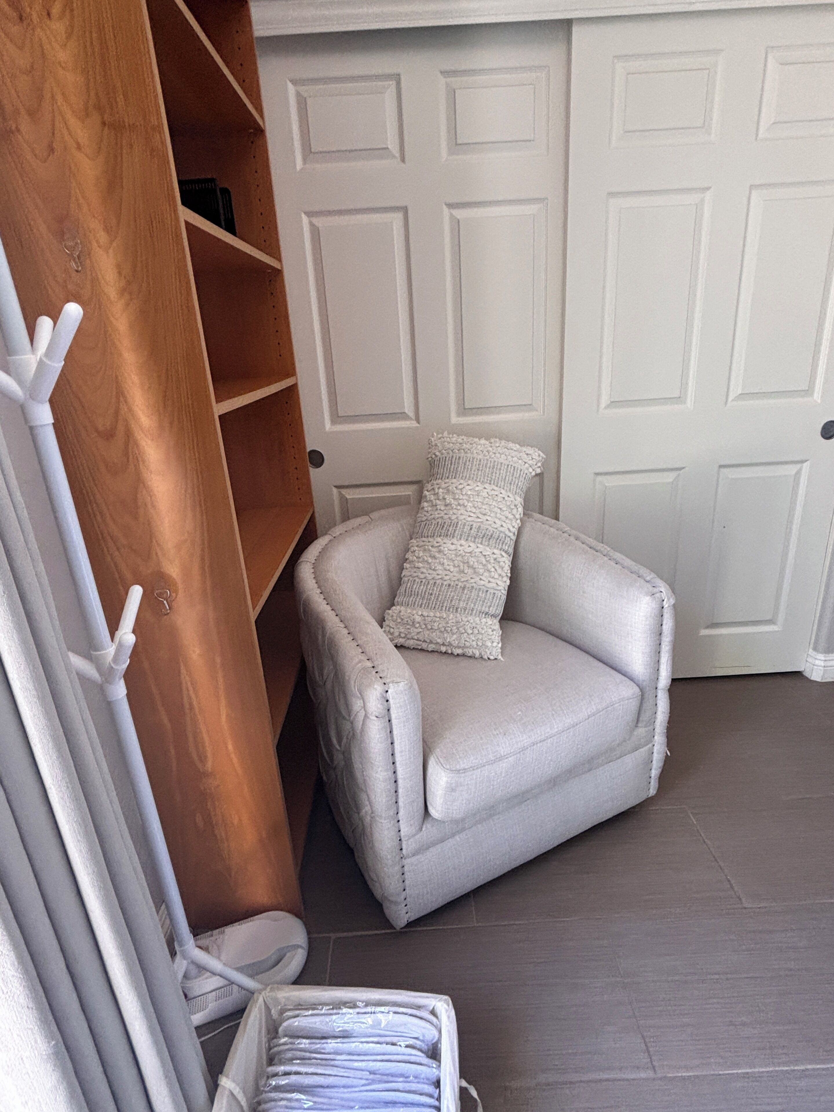 A corner room with a white chair, a wooden shelf, and a white door.