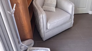 A corner room with a white chair, a wooden shelf, and a white door. - Your cozy getaway awaits in San Diego at this delightful house. (San Diego)