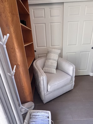 Una habitación de esquina con una silla blanca, un estante de madera y una puerta blanca.
